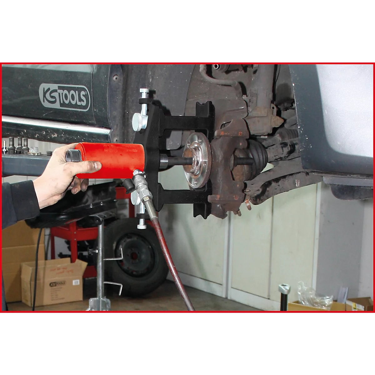 Eine Person nutzt ein Werkzeug, um ein Autoteil zu bearbeiten. Das Werkzeug ist rot, das Auto hat schwarze und silberne Teile.